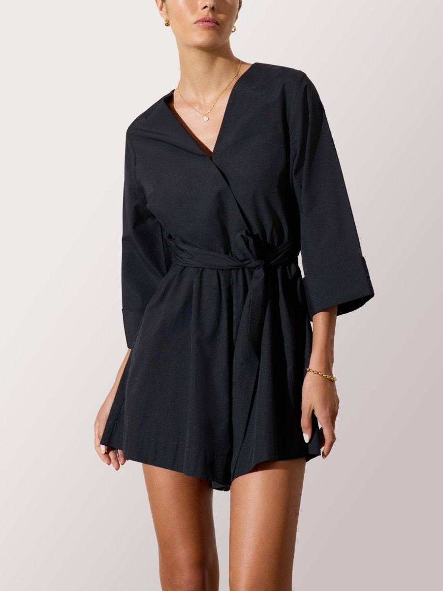 Women's black romper dress with a wrap-style front, belted waist, and three-quarter sleeves for a sleek, modern look.