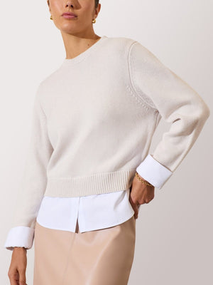 Cream sweater for women layered over a white shirt and paired with a beige leather skirt for a polished look.