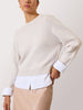 Cream sweater for women layered over a white shirt and paired with a beige leather skirt for a polished look.