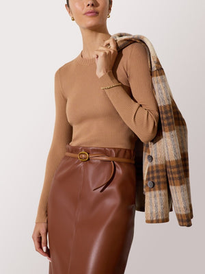 Women's brown ribbed sweater with long sleeves, styled with a leather skirt and plaid jacket draped over the shoulder.