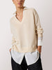 Women's layered collared shirt under sweater styled with a beige V-neck knit and dark wide-leg pants.