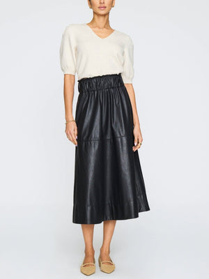 White V-neck sweater for women styled with a black faux leather skirt and beige flats.