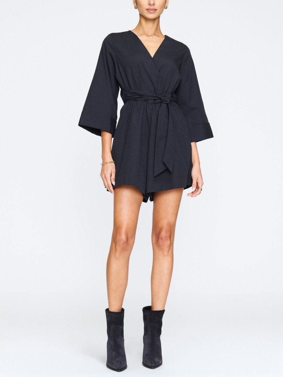 Black romper for women with a V-neckline, tie waist, wide sleeves, and paired with black suede ankle boots.