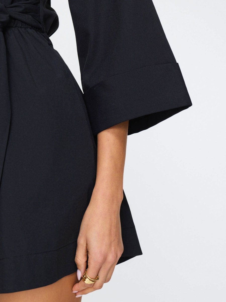 Women's black romper outfit featuring wide sleeves, a tied waist, and relaxed shorts for a modern and polished look.