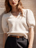 Women's V-neck sweater in ivory with short puff sleeves, paired with dark high-rise trousers and a tan belt.