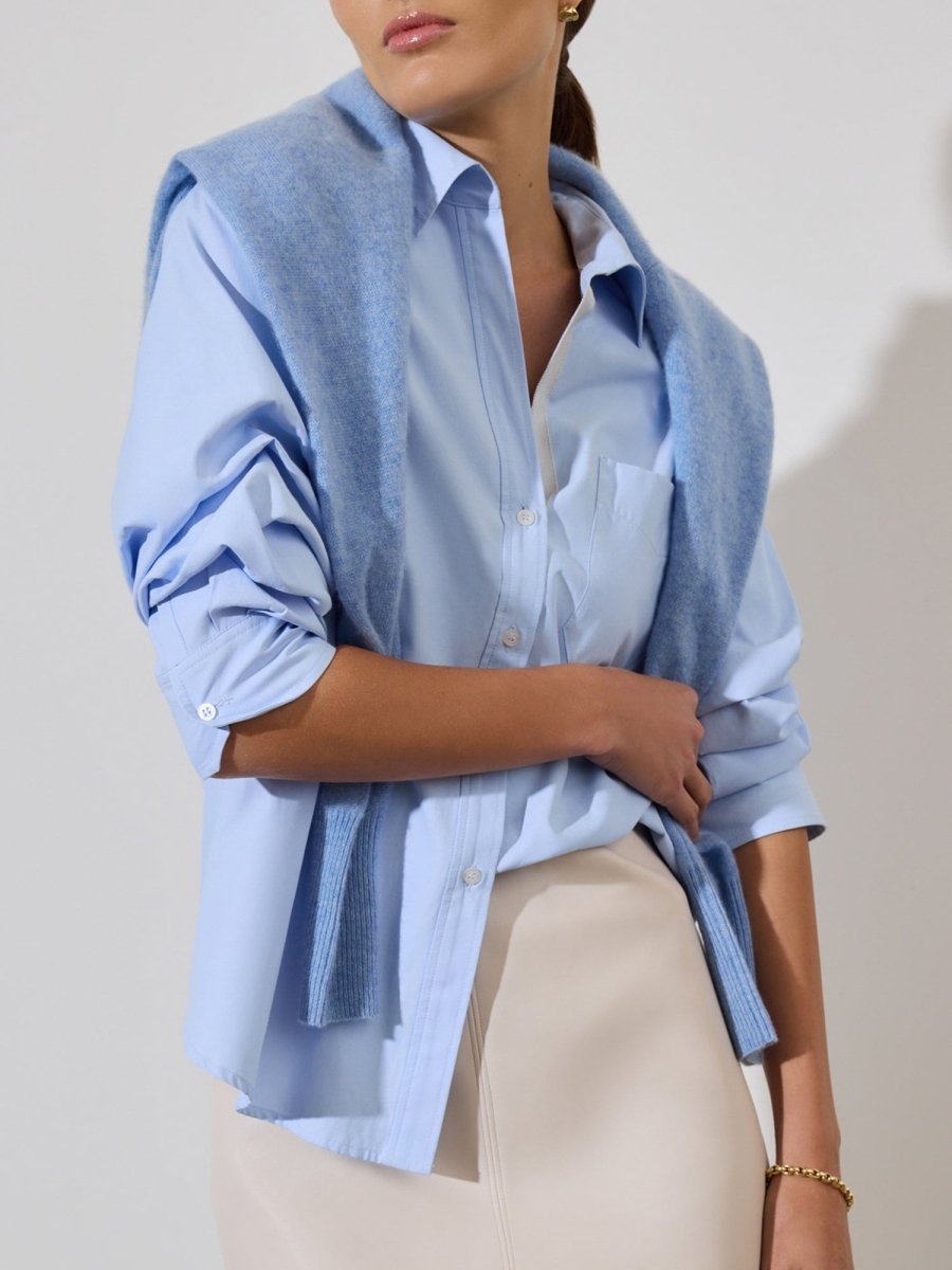 Women's blue button up shirt styled with a matching sweater draped over the shoulders and a beige skirt.