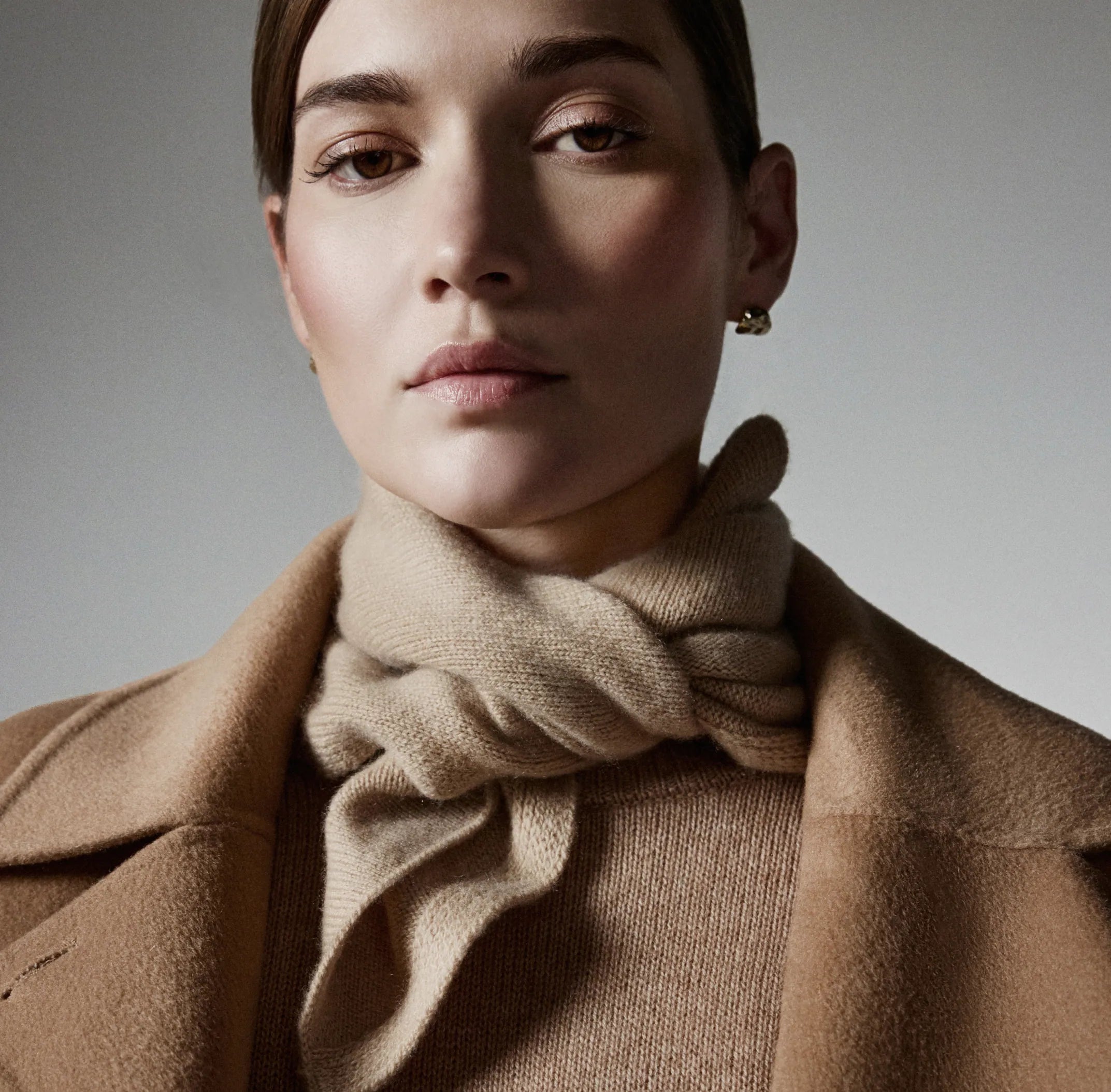 Woman wearing a brown coat and scarf against a neutral background