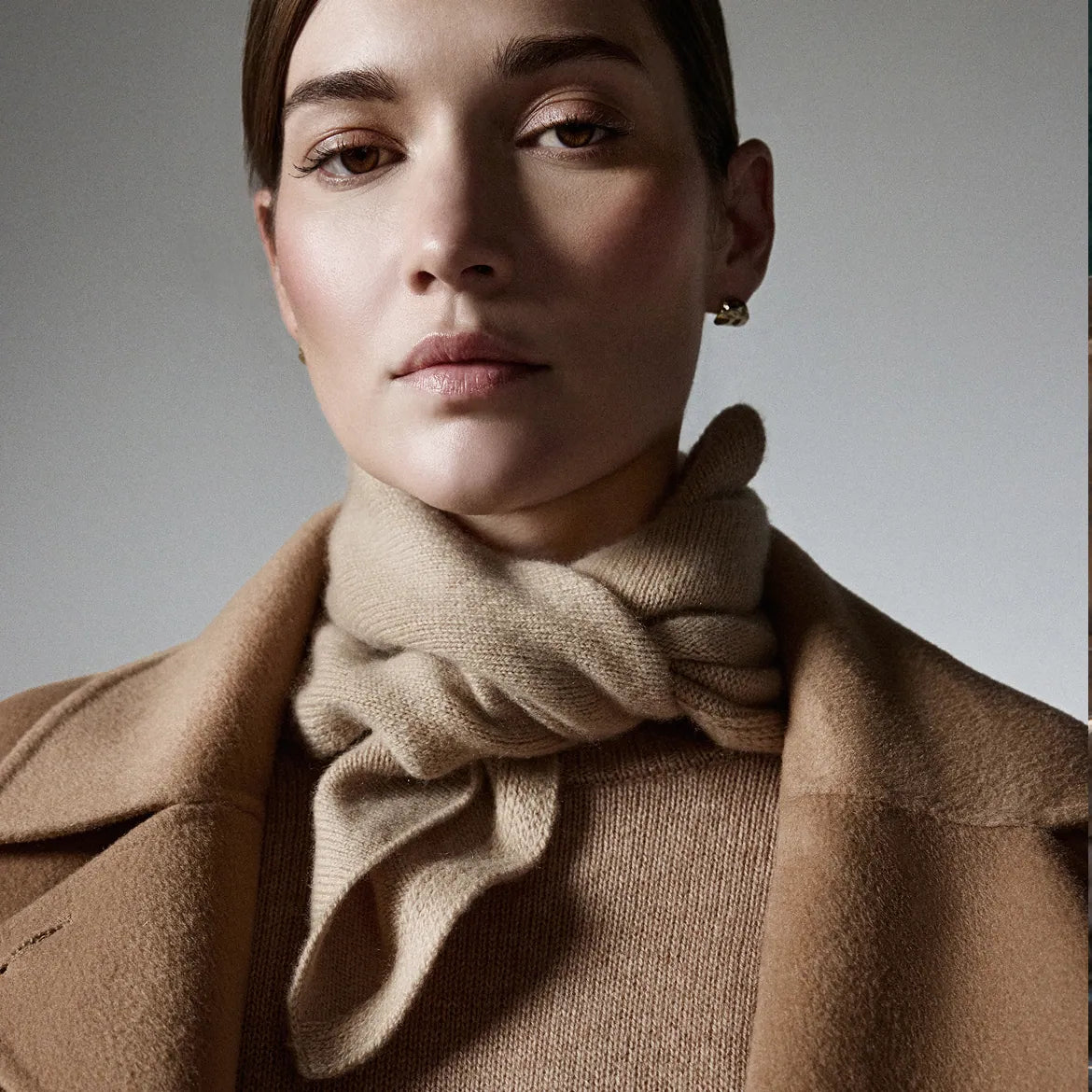 Woman wearing a brown coat and scarf against a neutral background