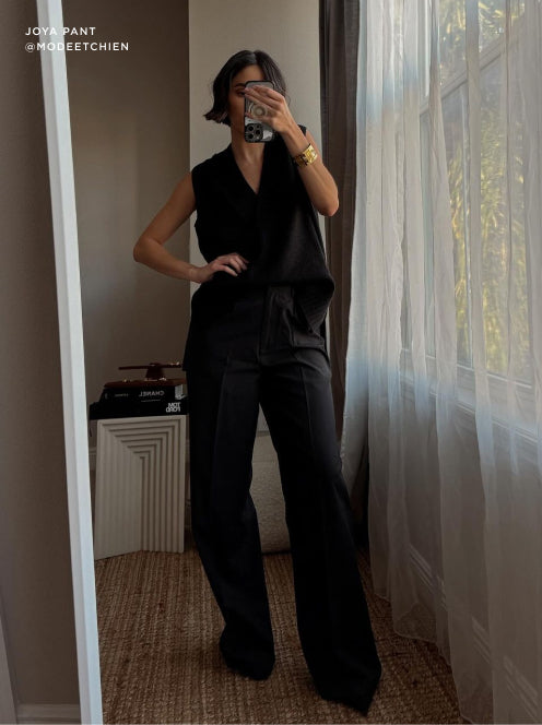 Monochrome black outfit featuring a sleeveless wrap top and high-waisted wide-leg trousers, styled with bold accessories for a sleek, modern edge.